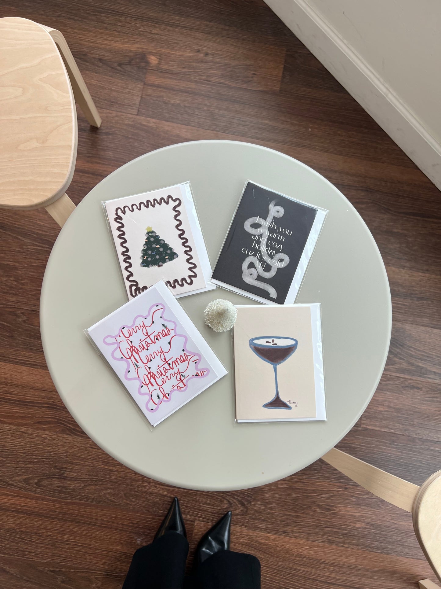Four greeting cards on a round table with wooden floor and chairs.